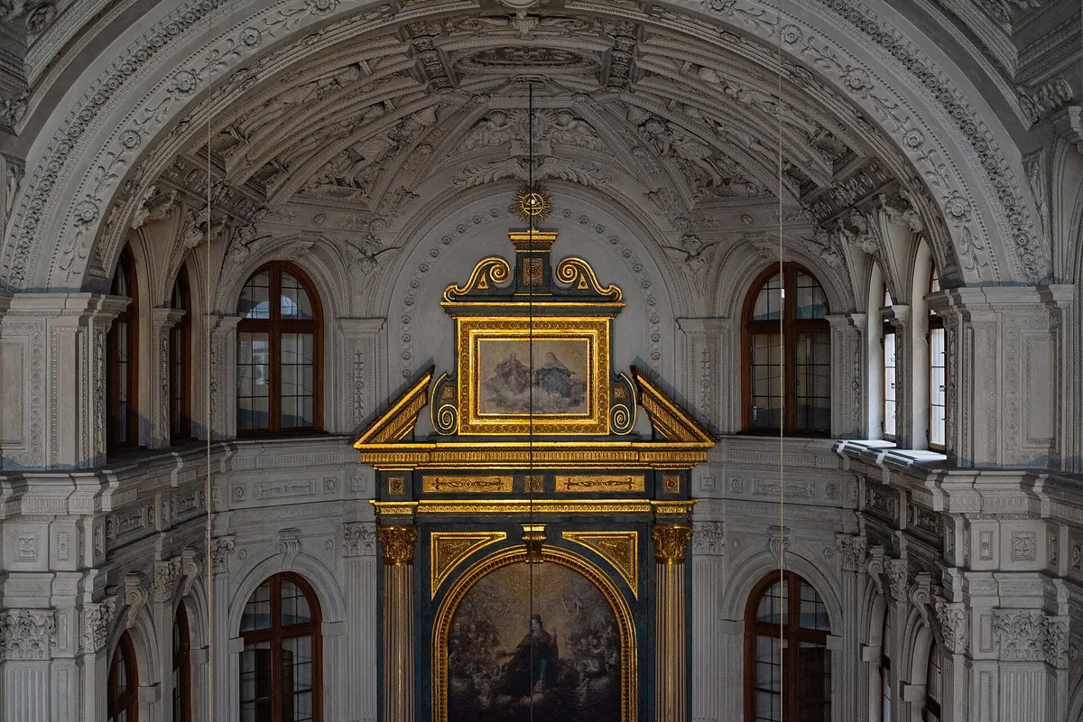 The gilded altar frame of the court chapel with a painting of the Virgin in glory, set between arched windows under a stucco vault.